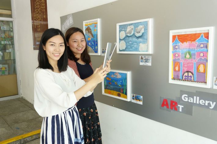 （左起）周子晴老師及劉珏琳老師親身示範如何使用 AR 觀看同學們整件作品。