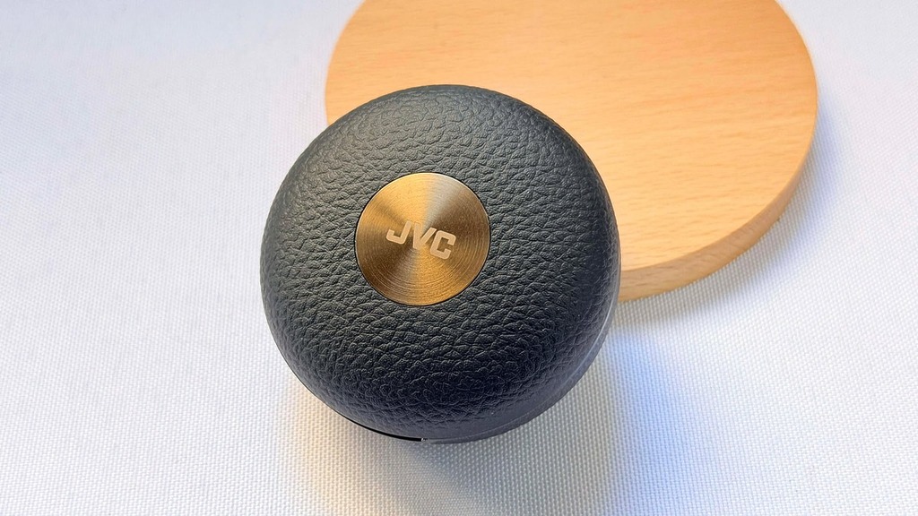 耳機的充電盒，在設計上有頗具心思，採用仿樂器盒的皮革質感外殼，並配上 JVC 品牌的金屬標誌作精緻點綴，帶點復古的味道。